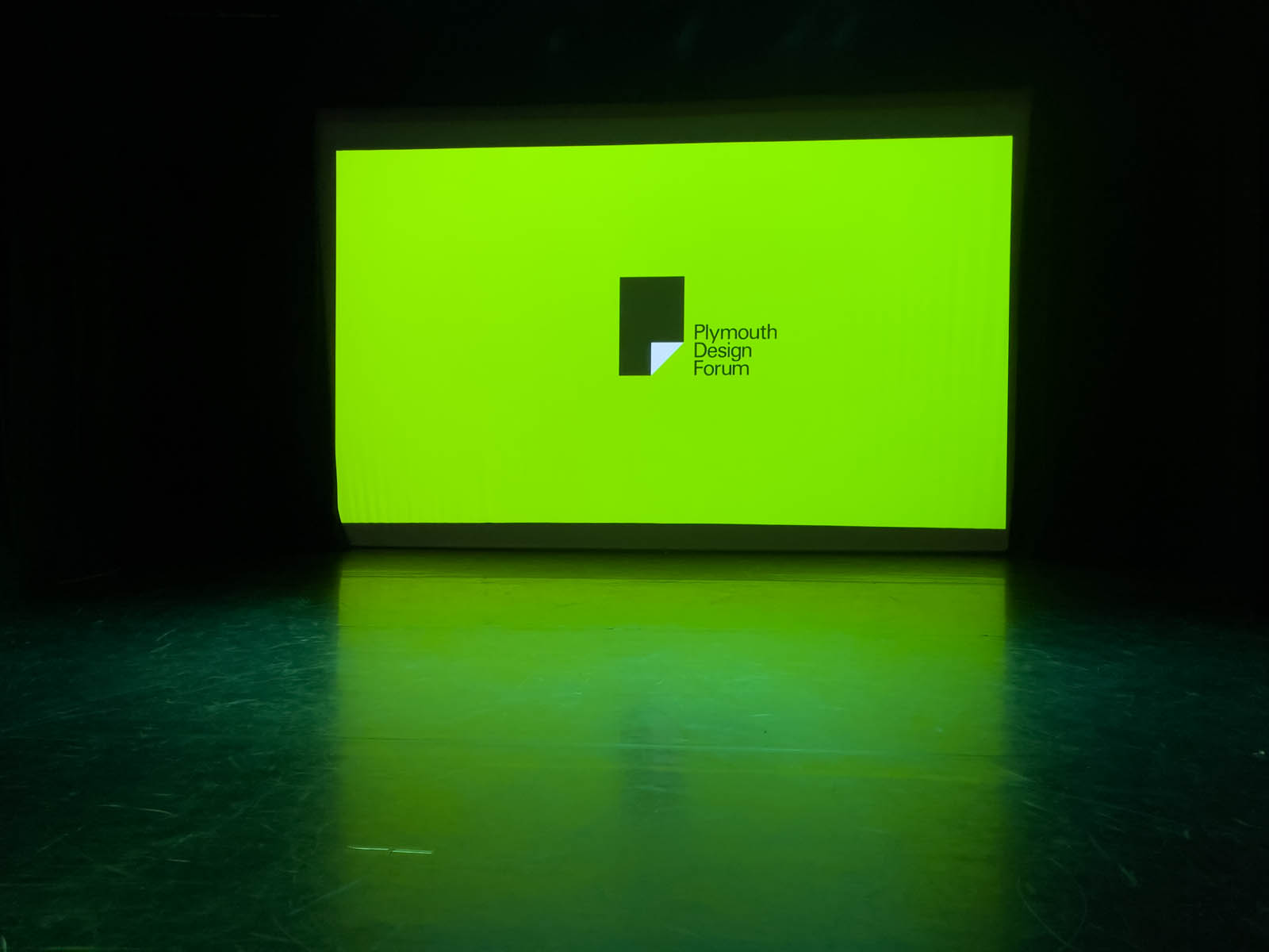 A large lime treen projection in a theatre . The text on screen reads "Plymouth Design Forum". Photo taken by Dennis Cook at an event where Plymouth and Exeter designers congregate.