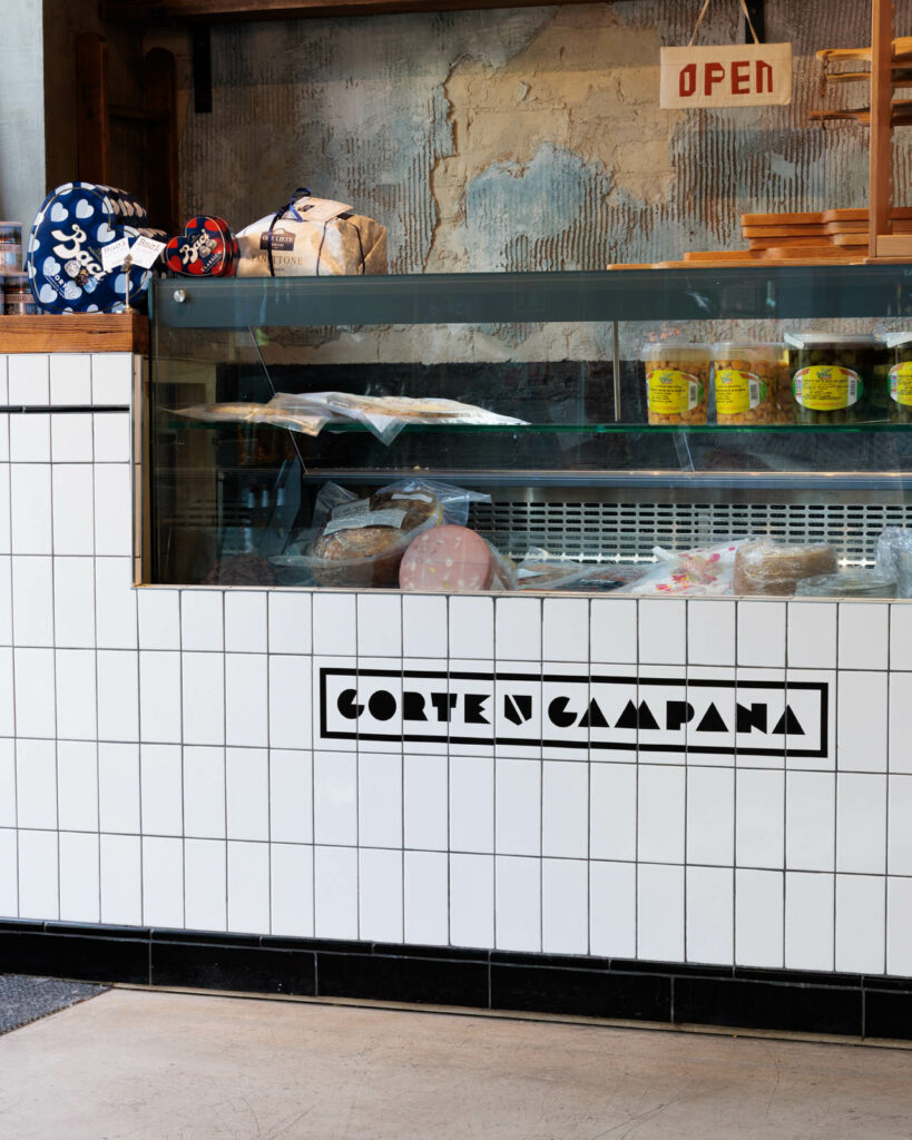 A tiled deli counter that features the Corte Campana restaurant logo design. There are Neapolitan foods on display.