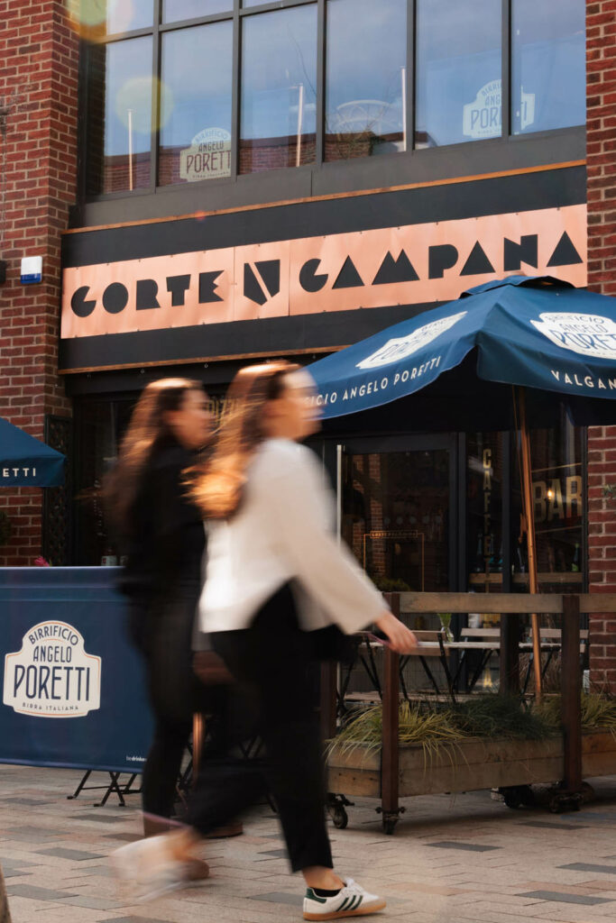 Two people walk past the parasols outside Corte Campana's restaurant in Stratford upon Avon. The weather is sunny. And example of how this Exeter design agency works with clients to create brands that stand out on crowded high streets across the UK.