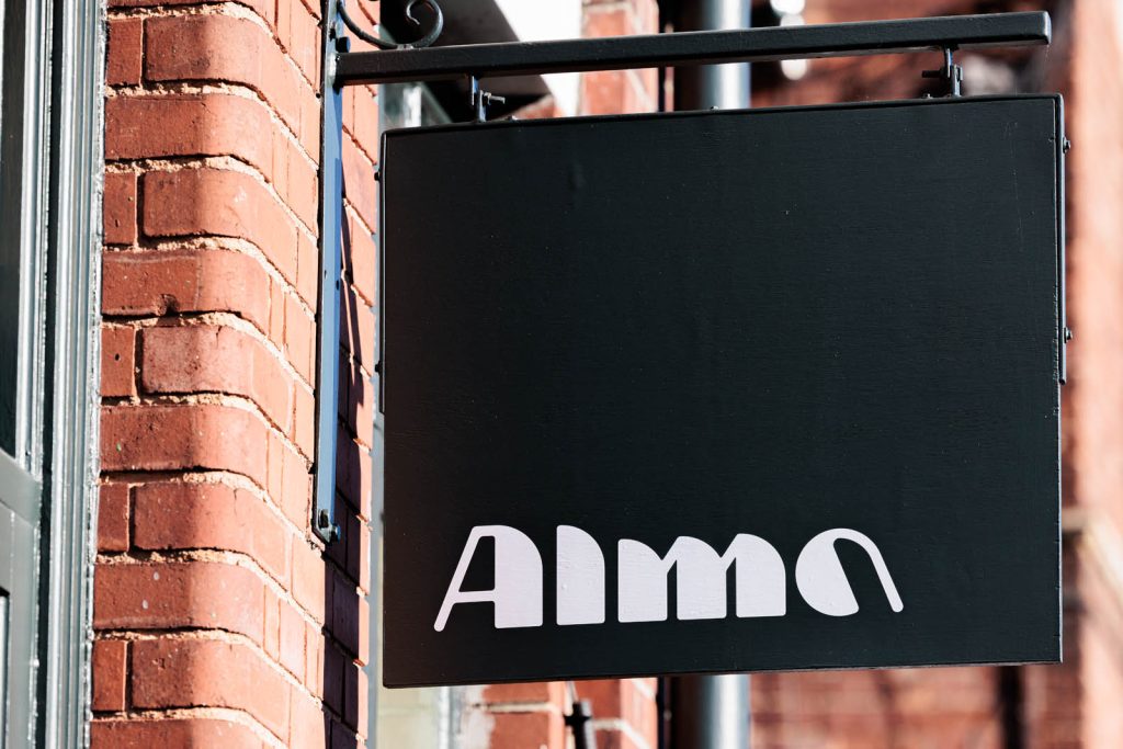 A close up photograph of a hanging sign with a logo word mark that reads "Alma" – an example of application from this coffee shop logo design project.