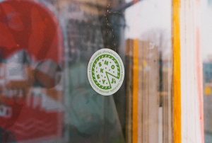 A circular sticker on a window. The sticker features a logo design for Smokey J's pizza truck, with type that reads "quality, sustainable, affordable wood fired pizza". The logo was produced by Devon design agency DC Design Works.