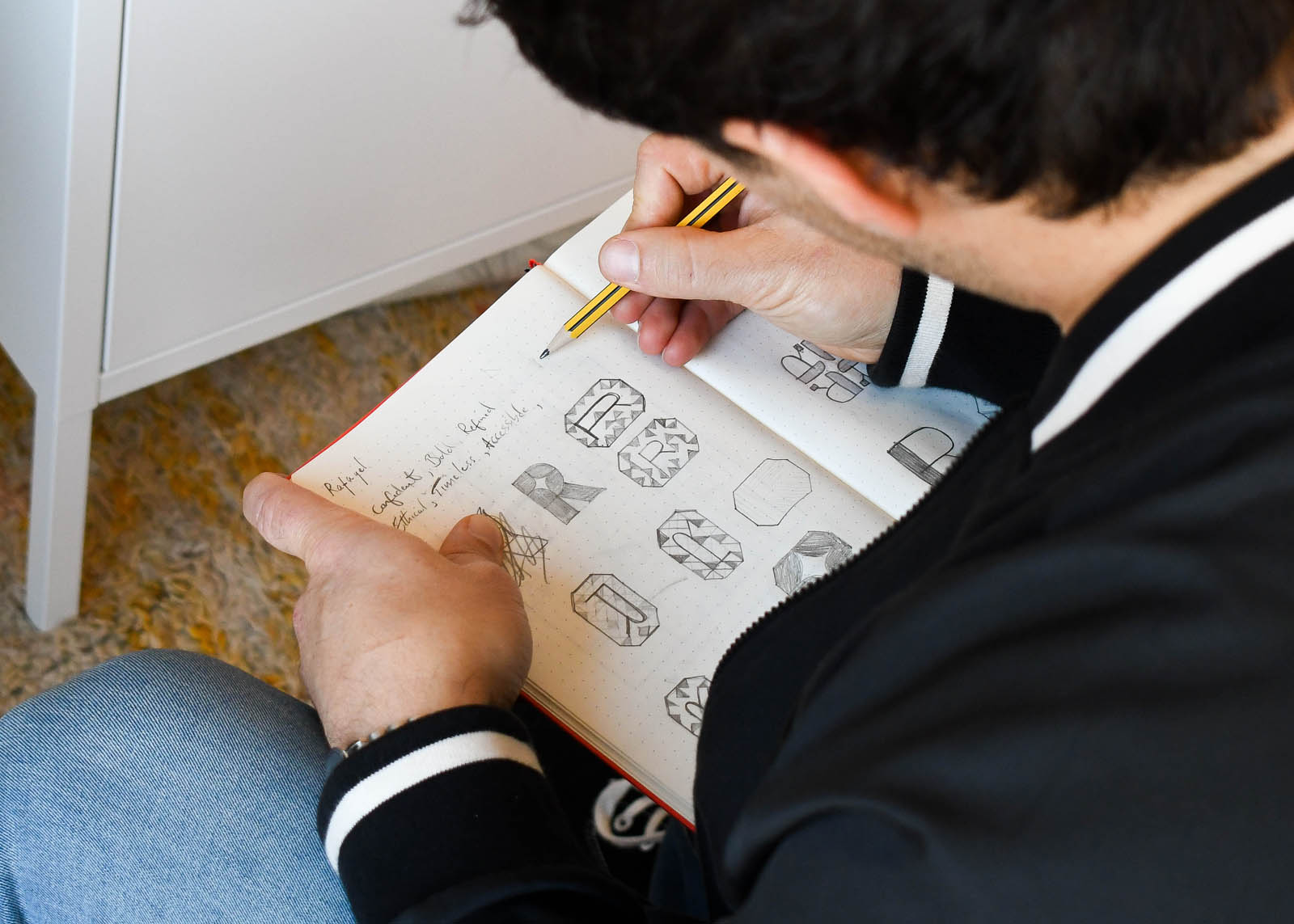 Exeter graphic designer Dennis Cook works on a new logo design sketch in a red notebook.