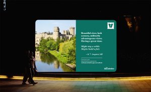 An example advertisement for Visit Warwickshire's logo and brand design project on a big screen.